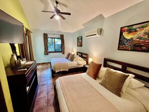 A hotel room with two beds, a ceiling fan, an air conditioning unit, a painting on the wall, and a window with curtains. - Seagull Cove Resort (Boca Chica)
