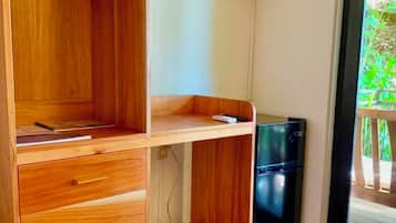 A room with a wooden desk, a television mounted on the wall, a small refrigerator, and a sliding glass door leading to an outdoor area.