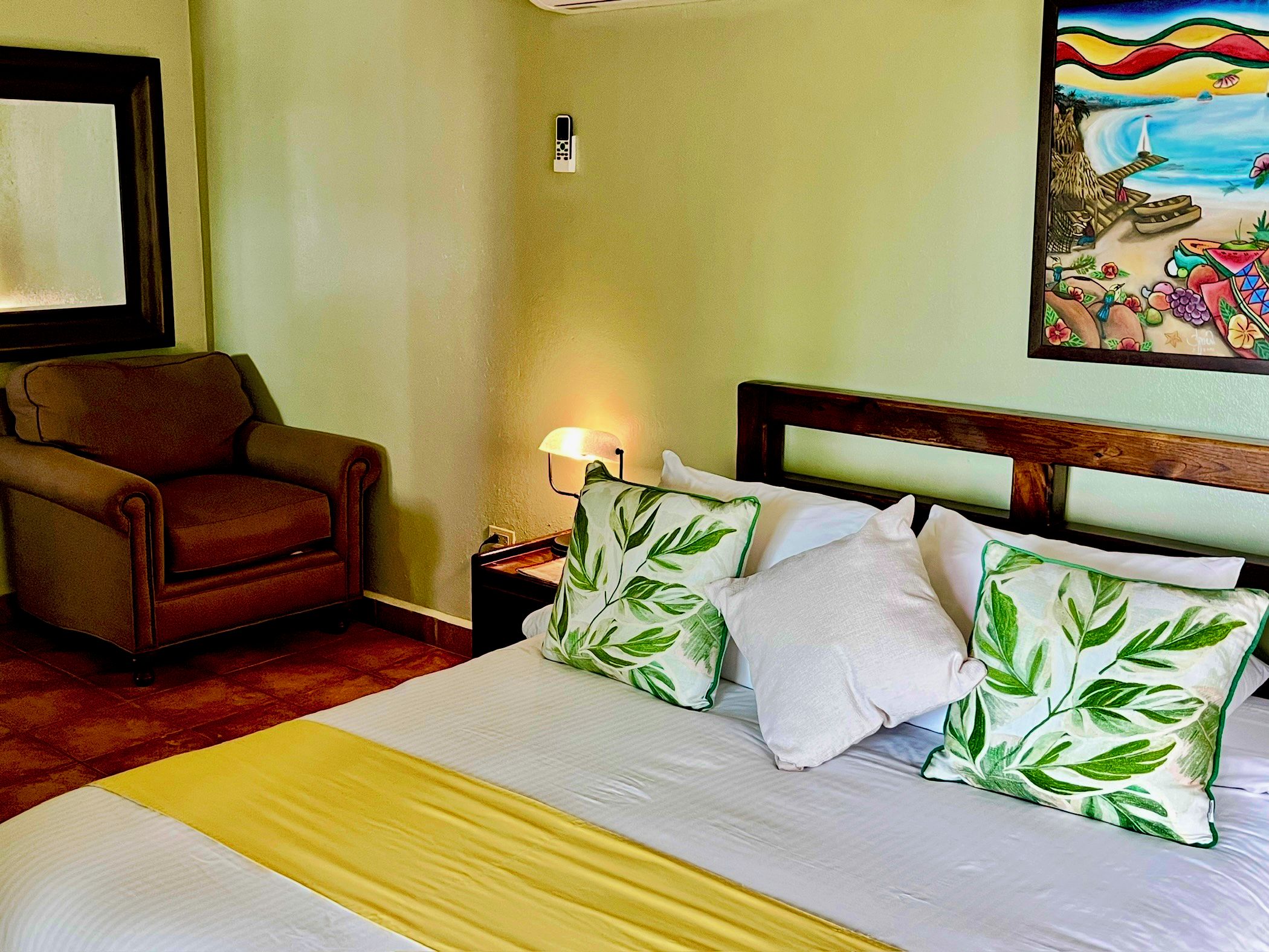 A hotel room with a bed, a chair, a nightstand, a lamp, and a painting on the wall.