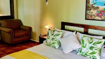 A hotel room with a bed, a chair, a nightstand, a lamp, and a painting on the wall.