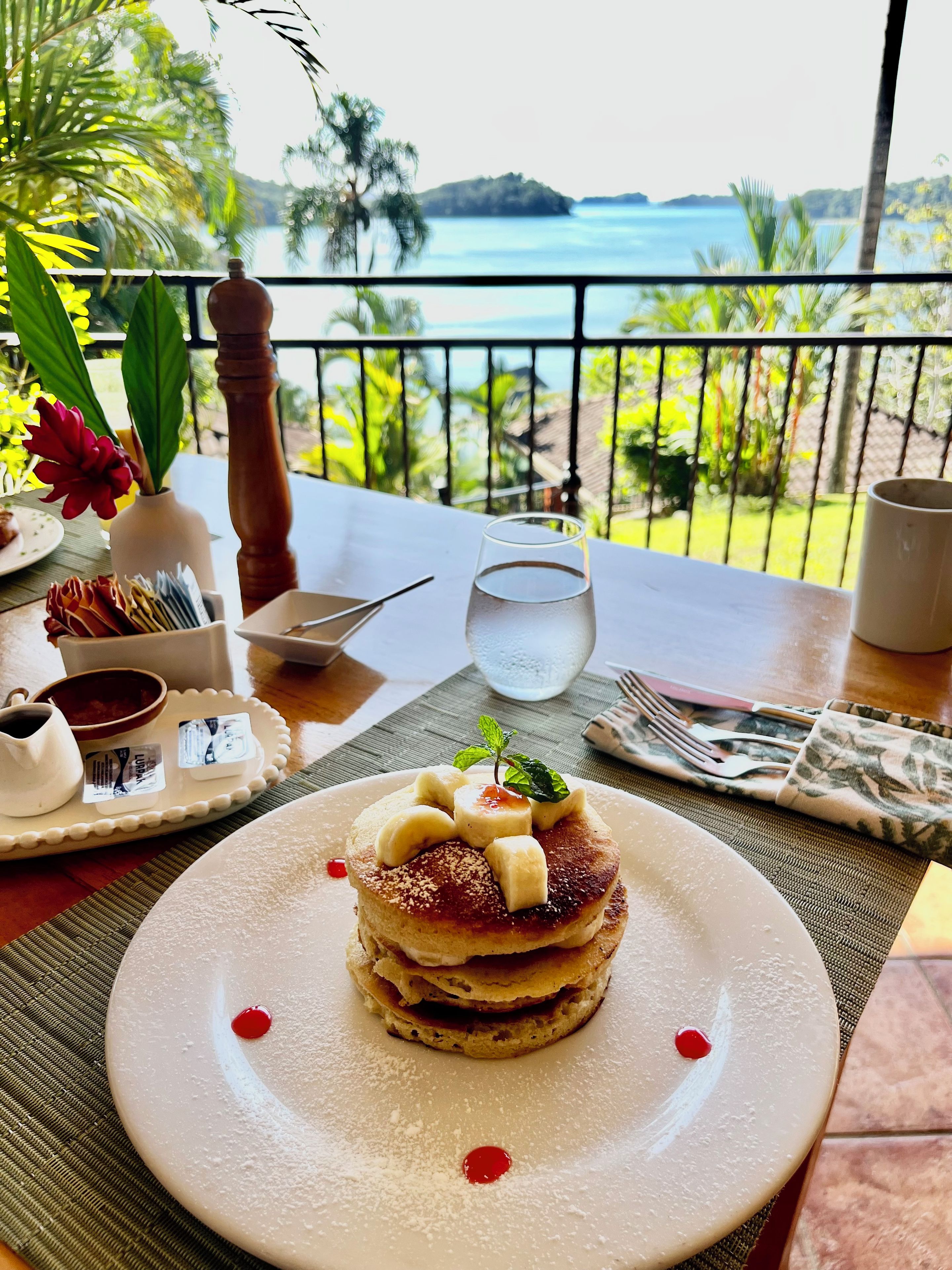 Una mesa con un plato de postre, un vaso de agua y vistas al mar.