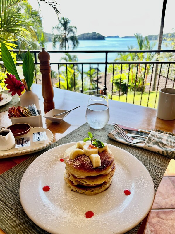 A table with a dessert plate, a glass of water, and a view of the sea.