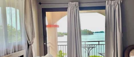 A bedroom with a bed, a view of the sea, and a balcony with a table and chairs.