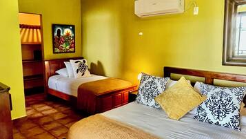 Una habitación de hotel con cama, mesitas de noche, aire acondicionado instalado en la pared y un cuadro.