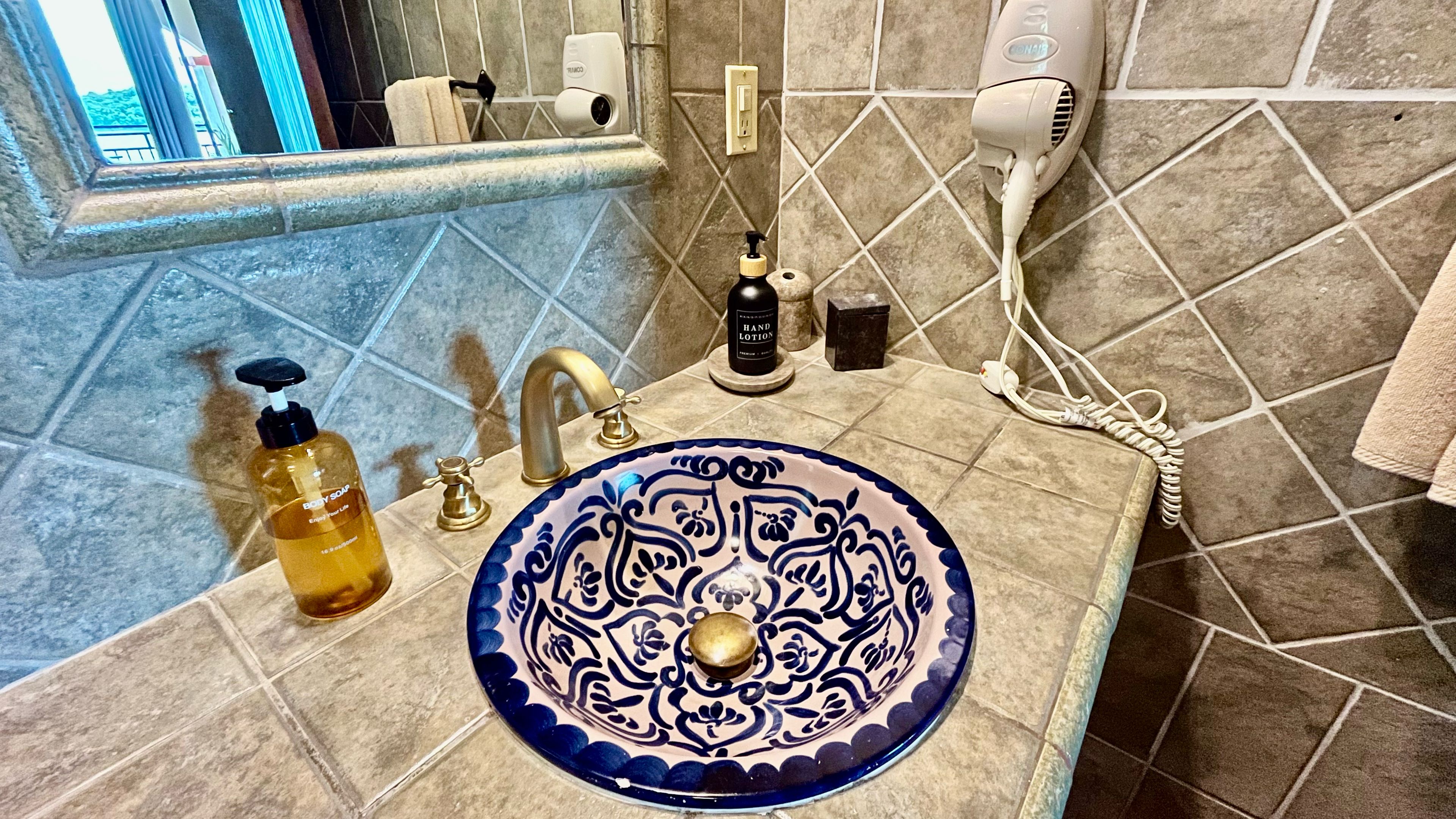 Un baño con lavamanos, jabón de manos, secador de pelo y botella de loción.