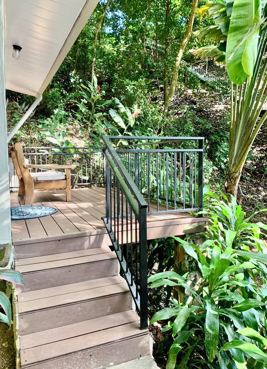 A wooden deck with a metal railing leading to a covered porch area.