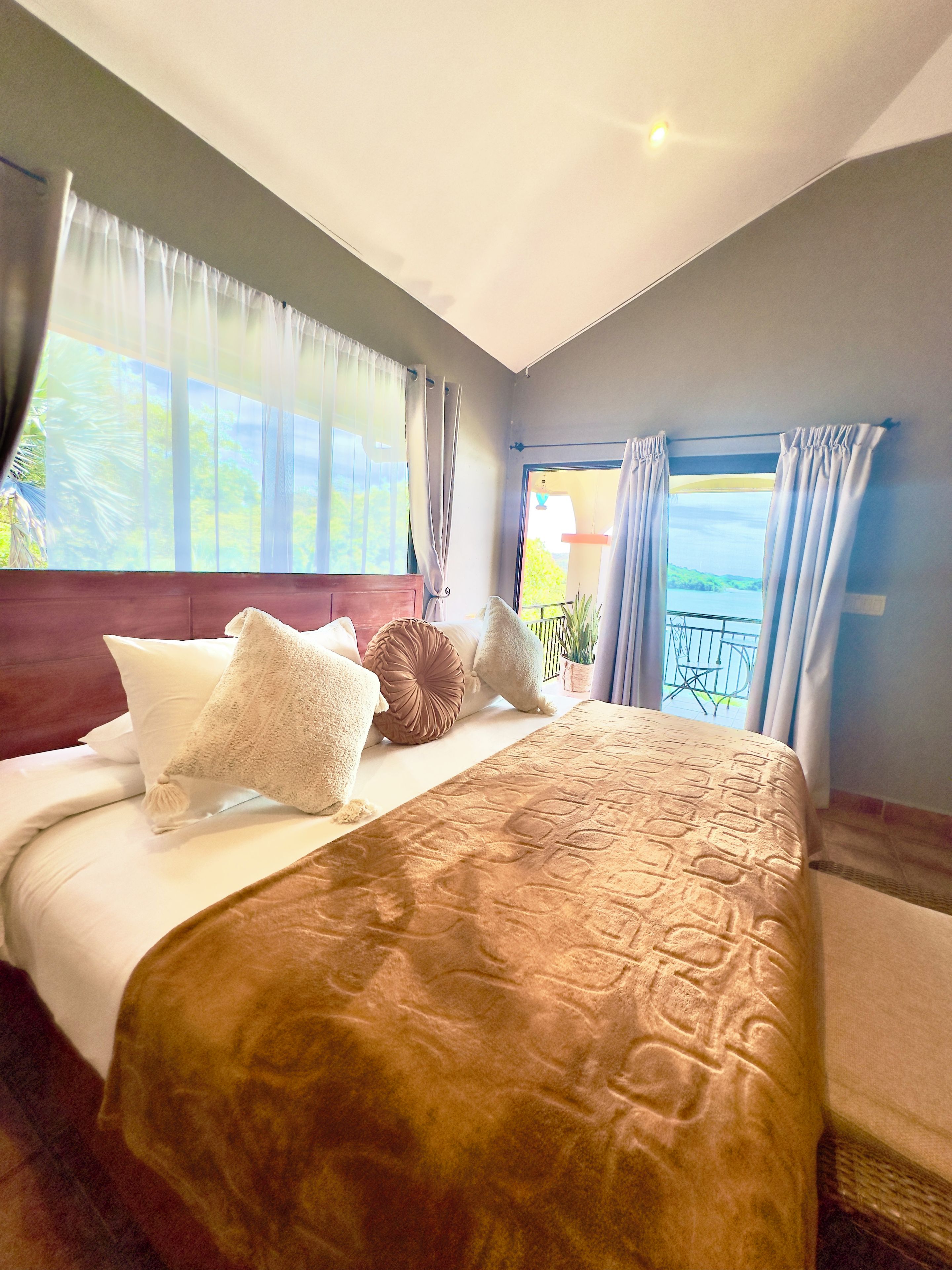 Habitación de hotel con una cama grande, vistas al exterior y un balcón con barandilla.