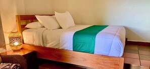 A bed with white bedding and a green throw, a nightstand with a lamp, and a wicker chair. - Seagull Cove Resort (Boca Chica)