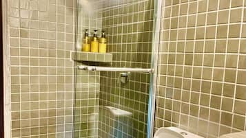 A bathroom with a glass-enclosed shower, a toilet, and a shelf with toiletries.