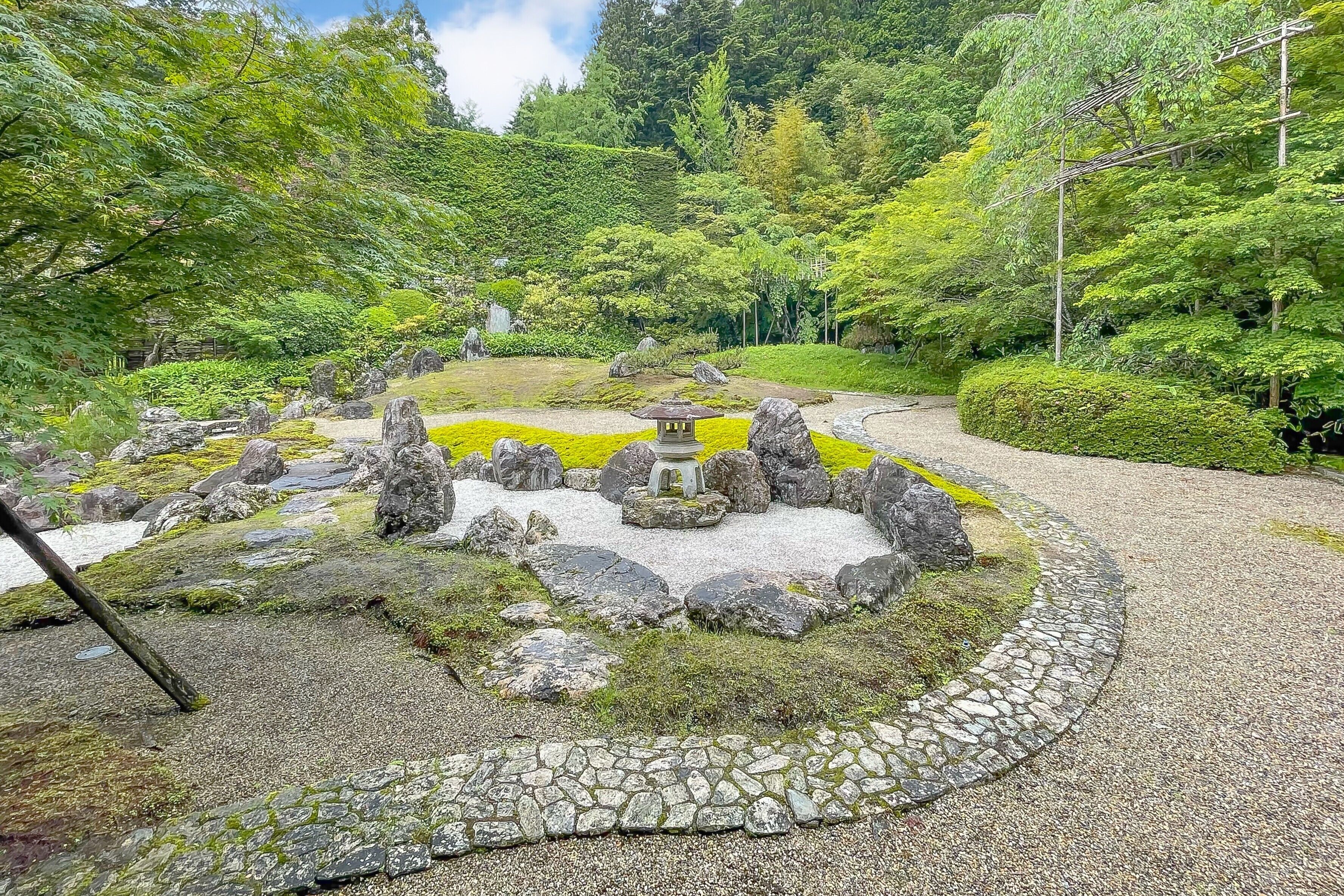 A traditional Japanese garden with a stone pathway, moss-covered rocks, and a small wooden lantern.