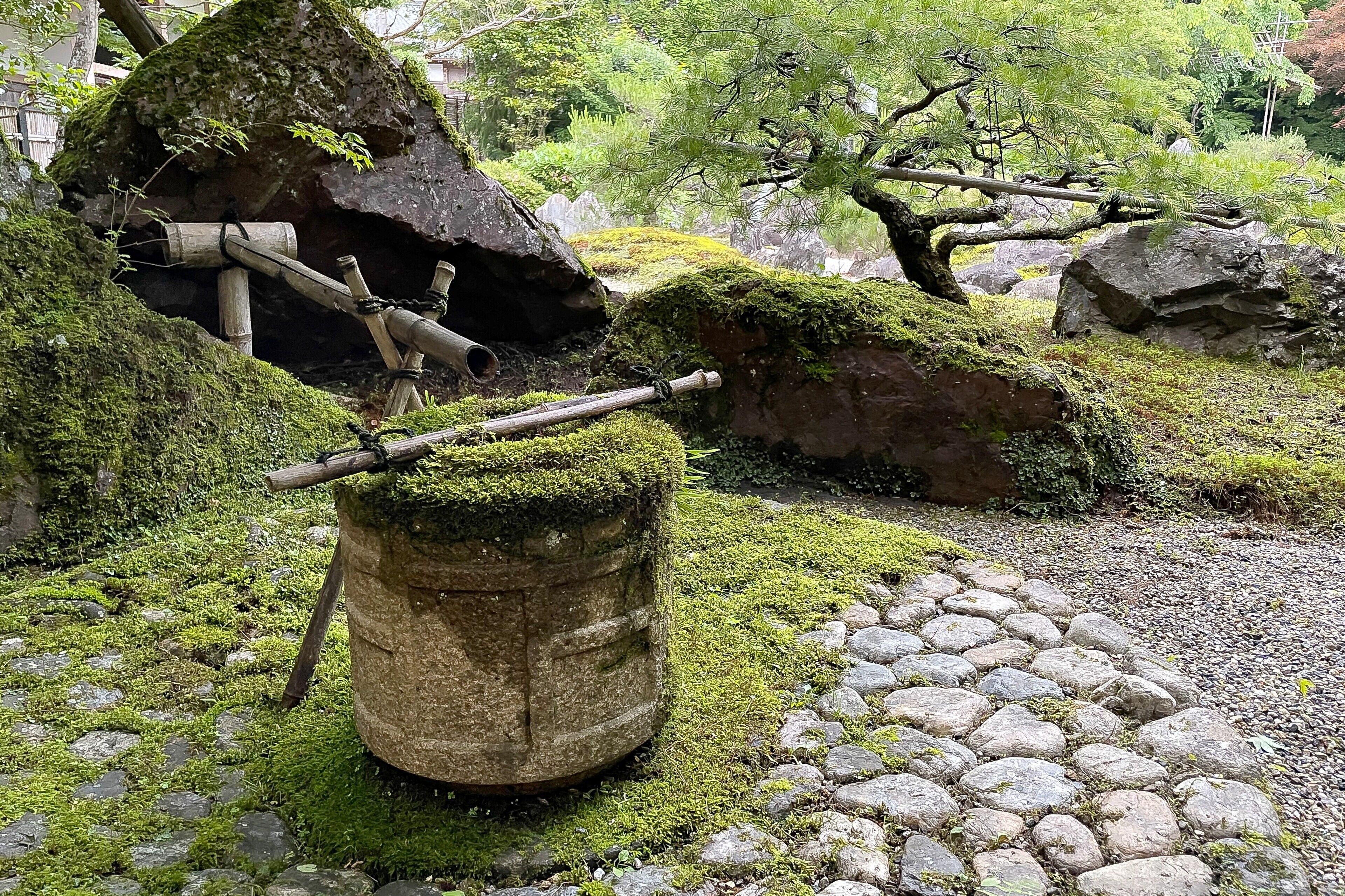Un jardín con rocas cubiertas de musgo, un sendero de piedra y estructuras de madera.