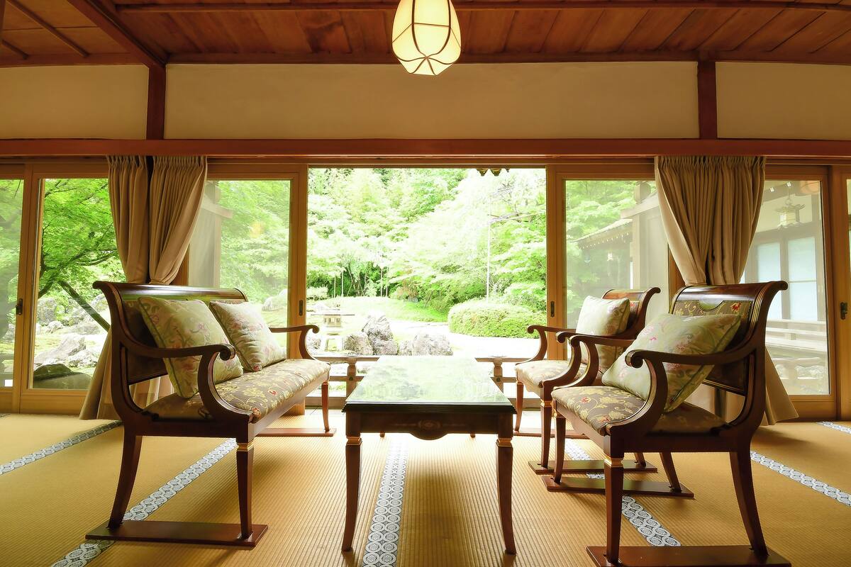 A traditional Japanese room with tatami flooring, a low table, and four wooden chairs with cushions.