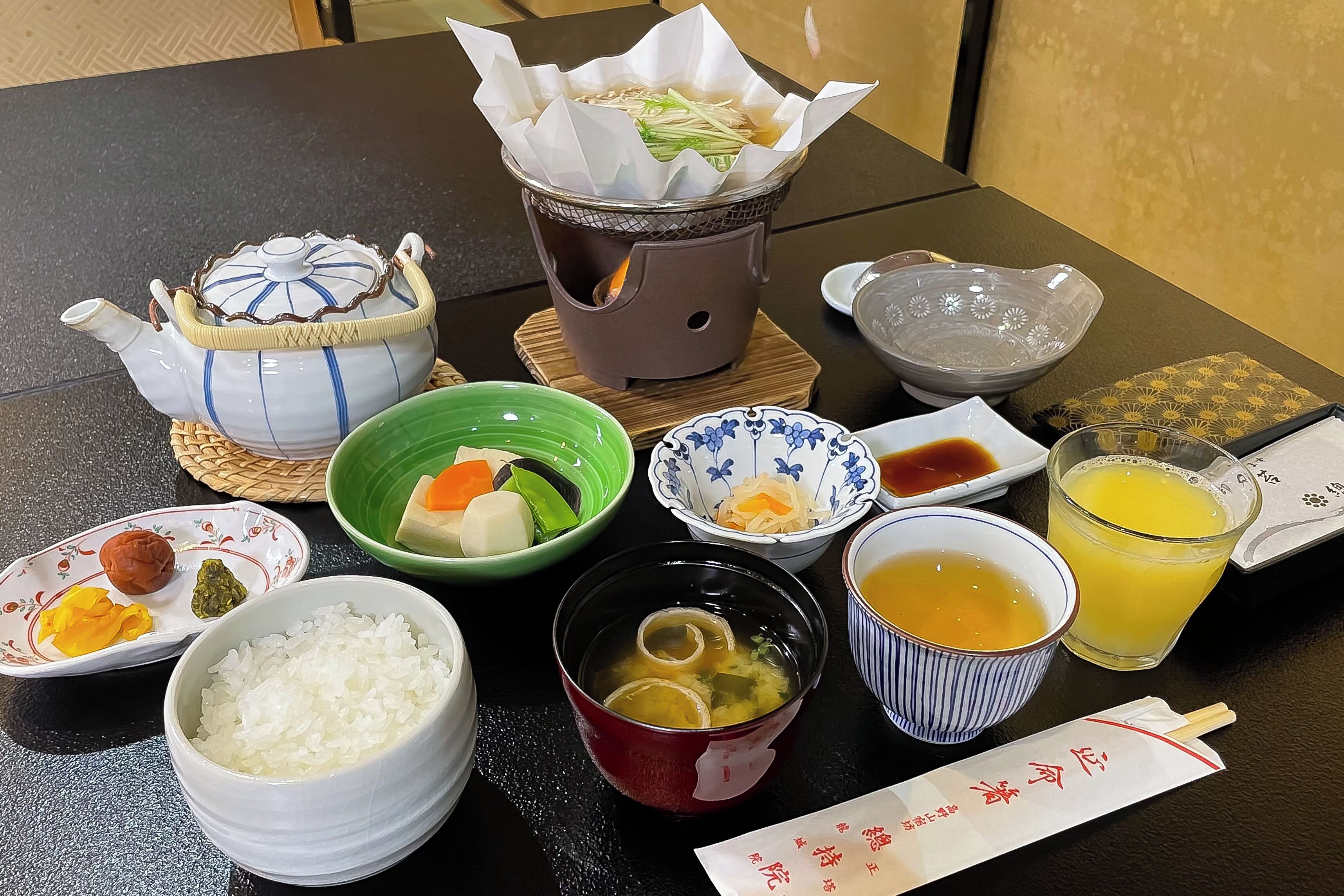 Une table où l’on trouve divers plats, notamment du riz, de la soupe et un plat mijoté servi à table.