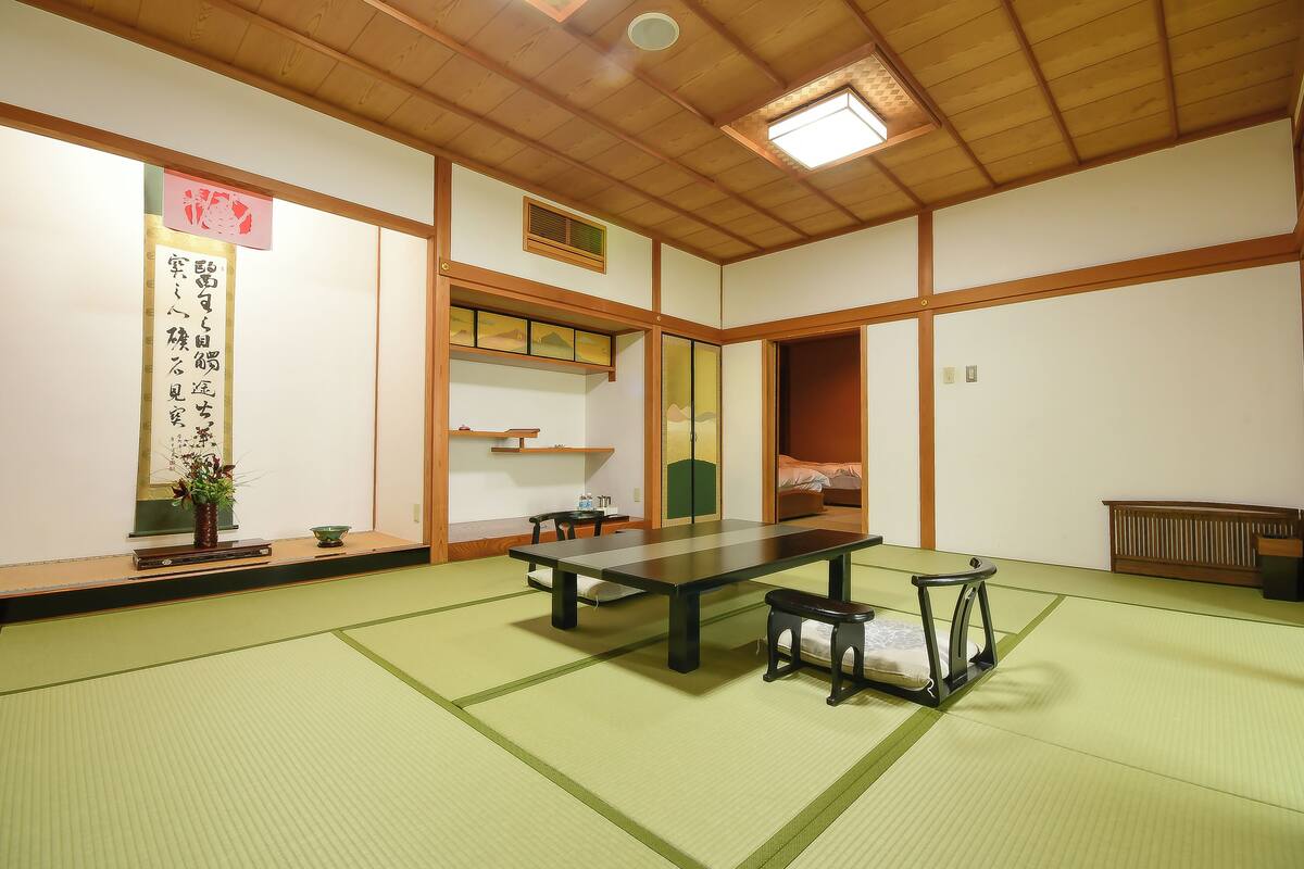 A traditional Japanese room with tatami flooring, a low table, a bench, and a sliding door.