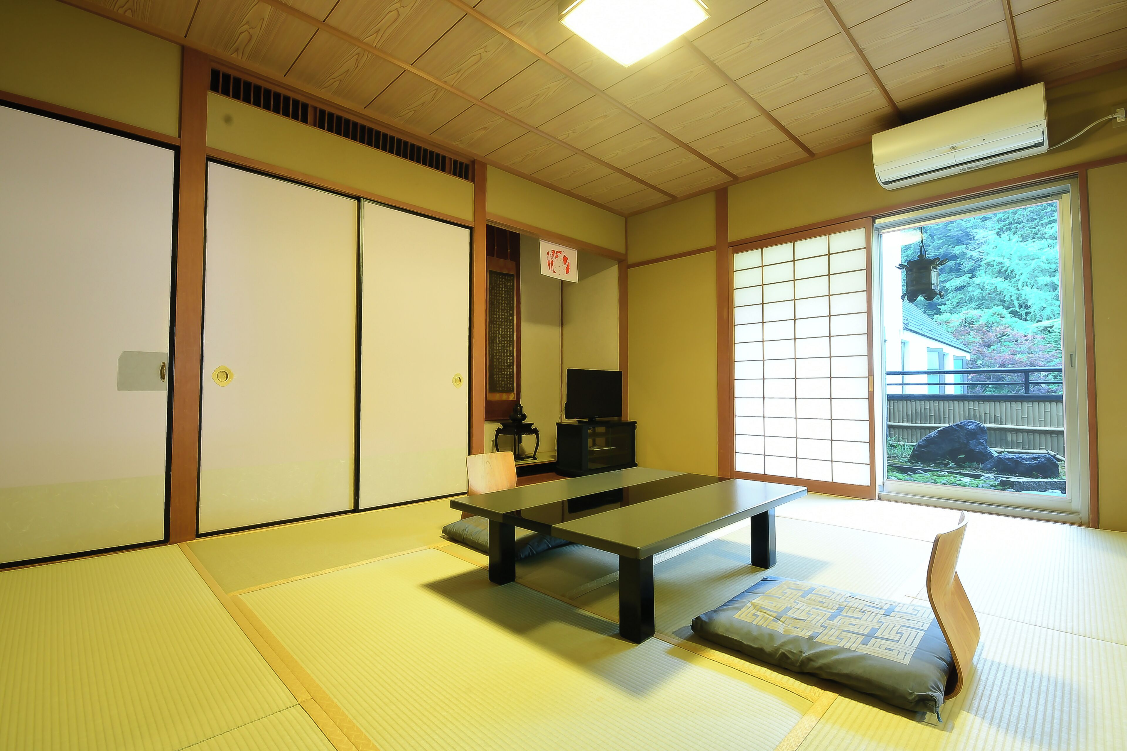 A traditional Japanese room with tatami flooring, a low table, sliding doors, and a view of a garden.