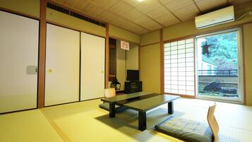 A traditional Japanese room with tatami flooring, a low table, sliding doors, and a view of a garden.