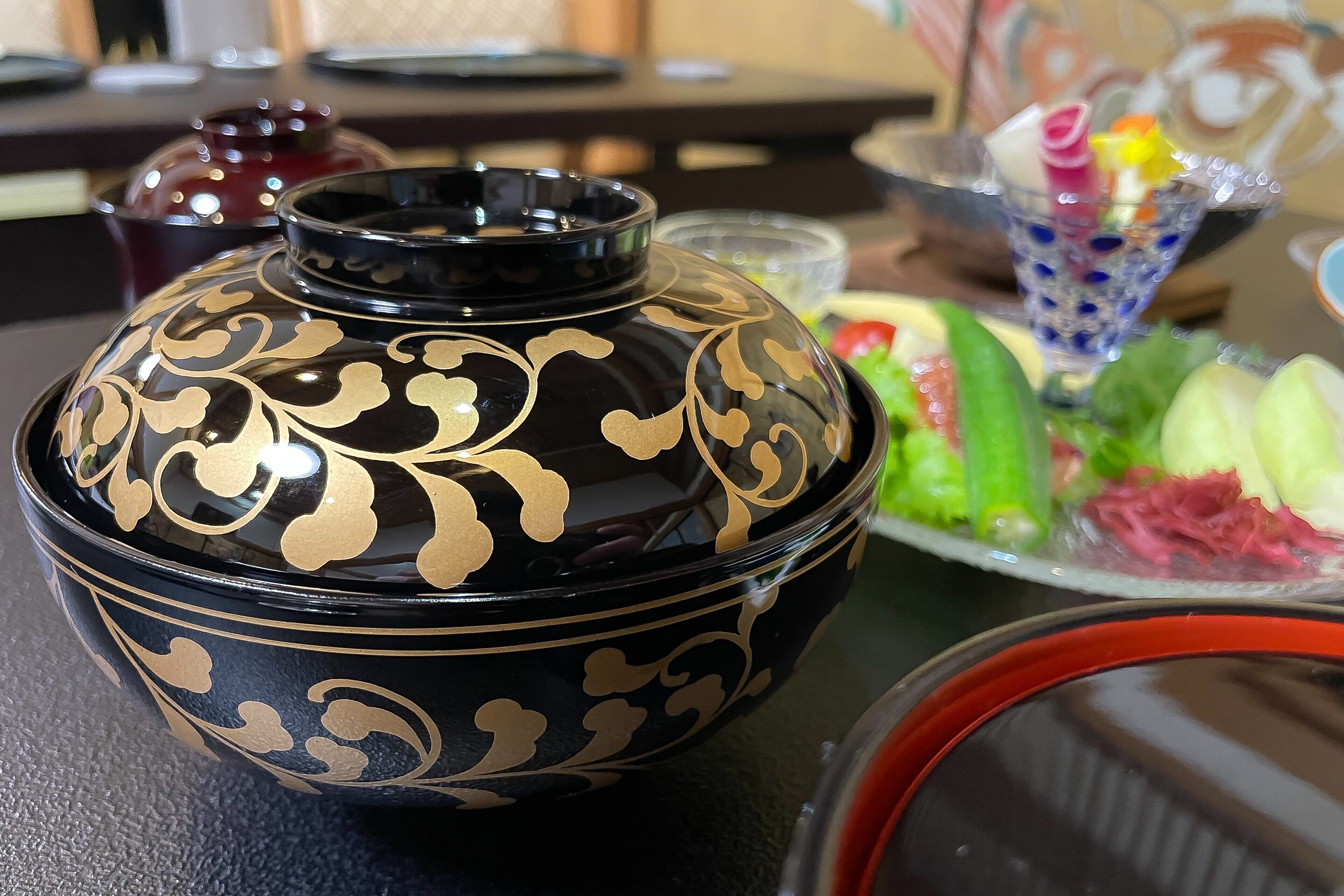 A black and gold decorative bowl on a table with a salad and a glass of bubble tea.