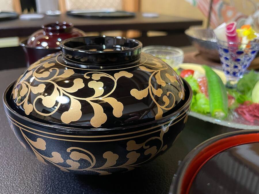 A black and gold decorative bowl on a table with a salad and a glass of bubble tea.