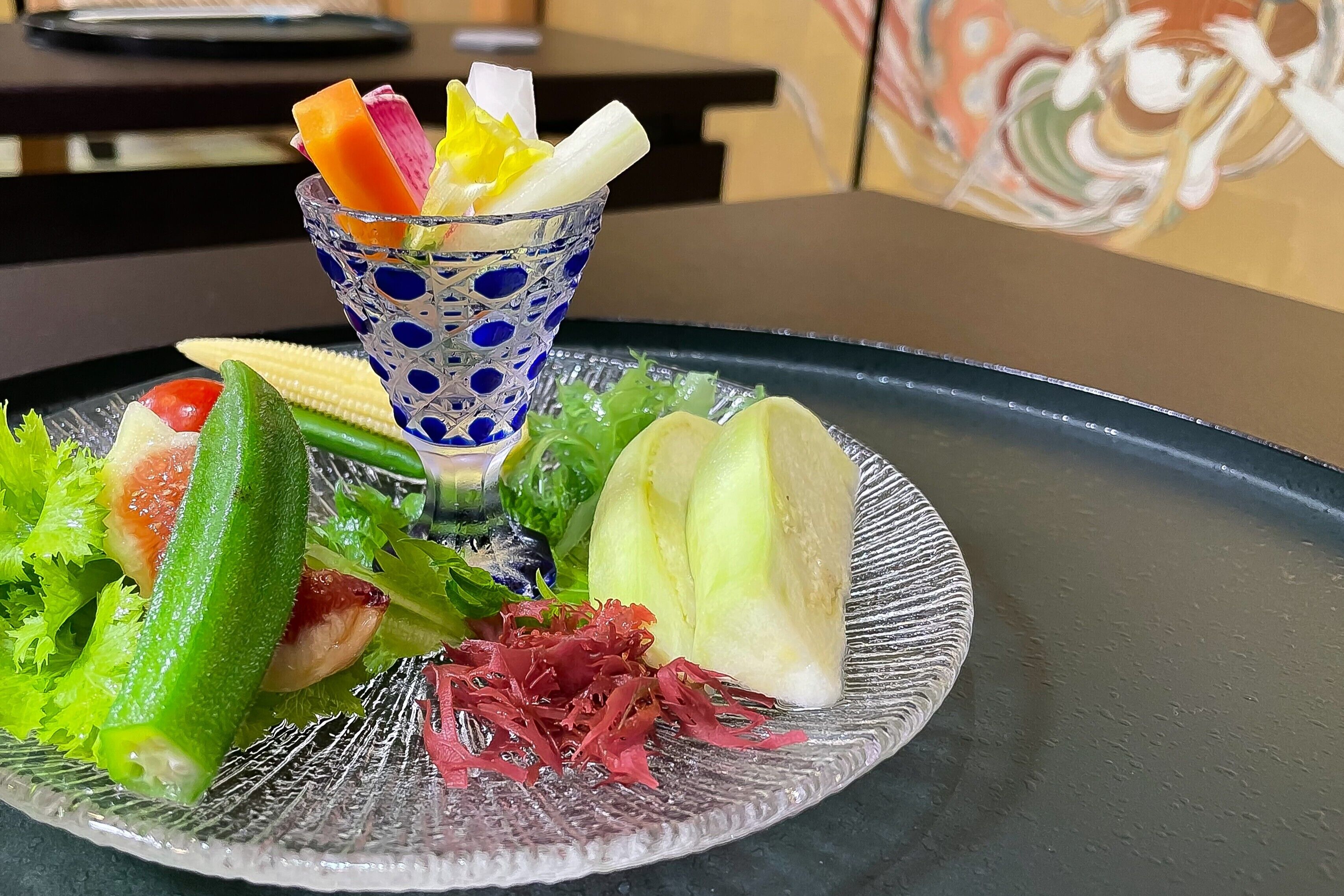 A glass plate with various vegetables and a decorative glass.