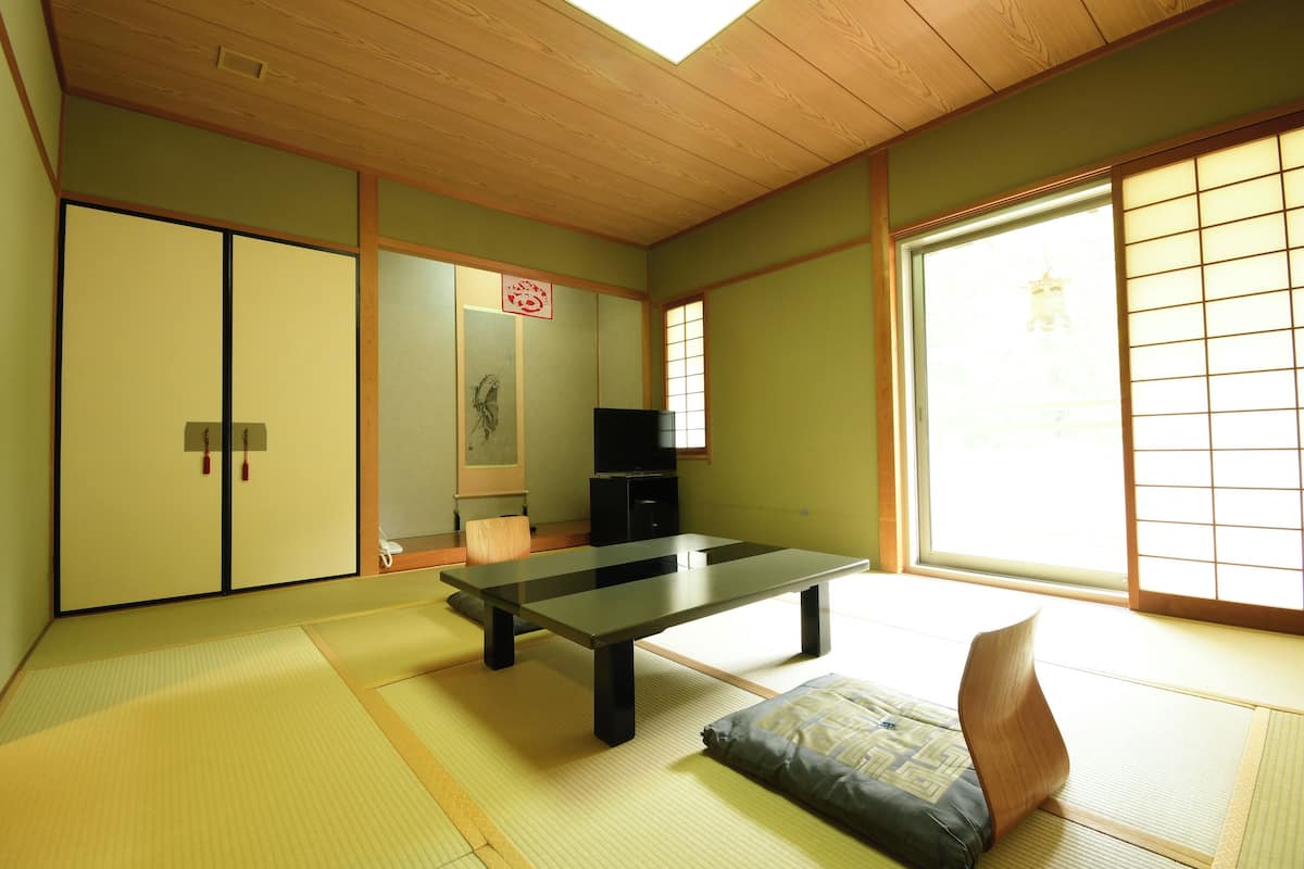A traditional Japanese room with tatami flooring, a low table, sliding doors, and a large window with shoji screens.