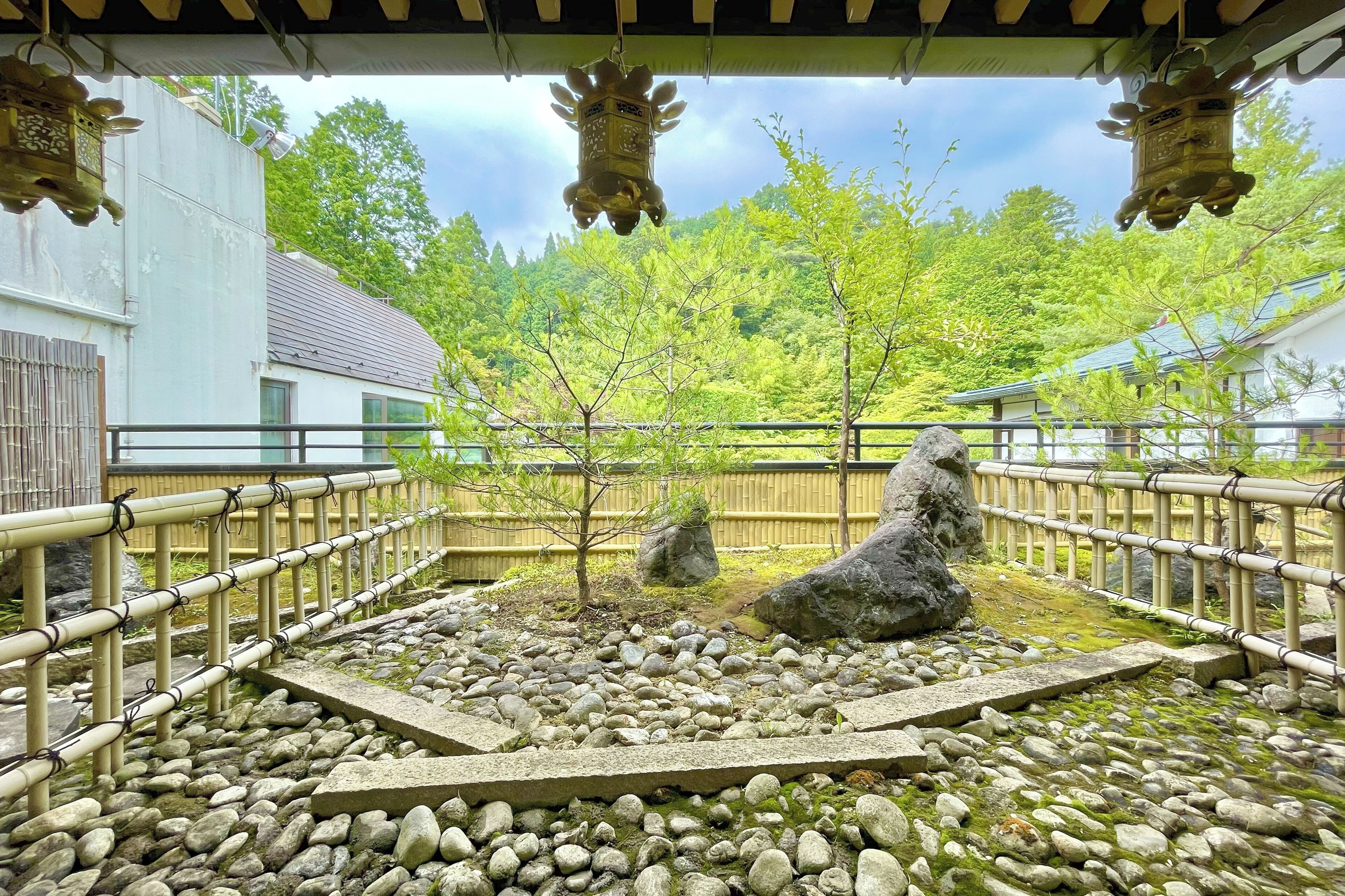 Un jardín japonés tradicional con un farol de piedra, una cerca de bambú y un pequeño árbol.