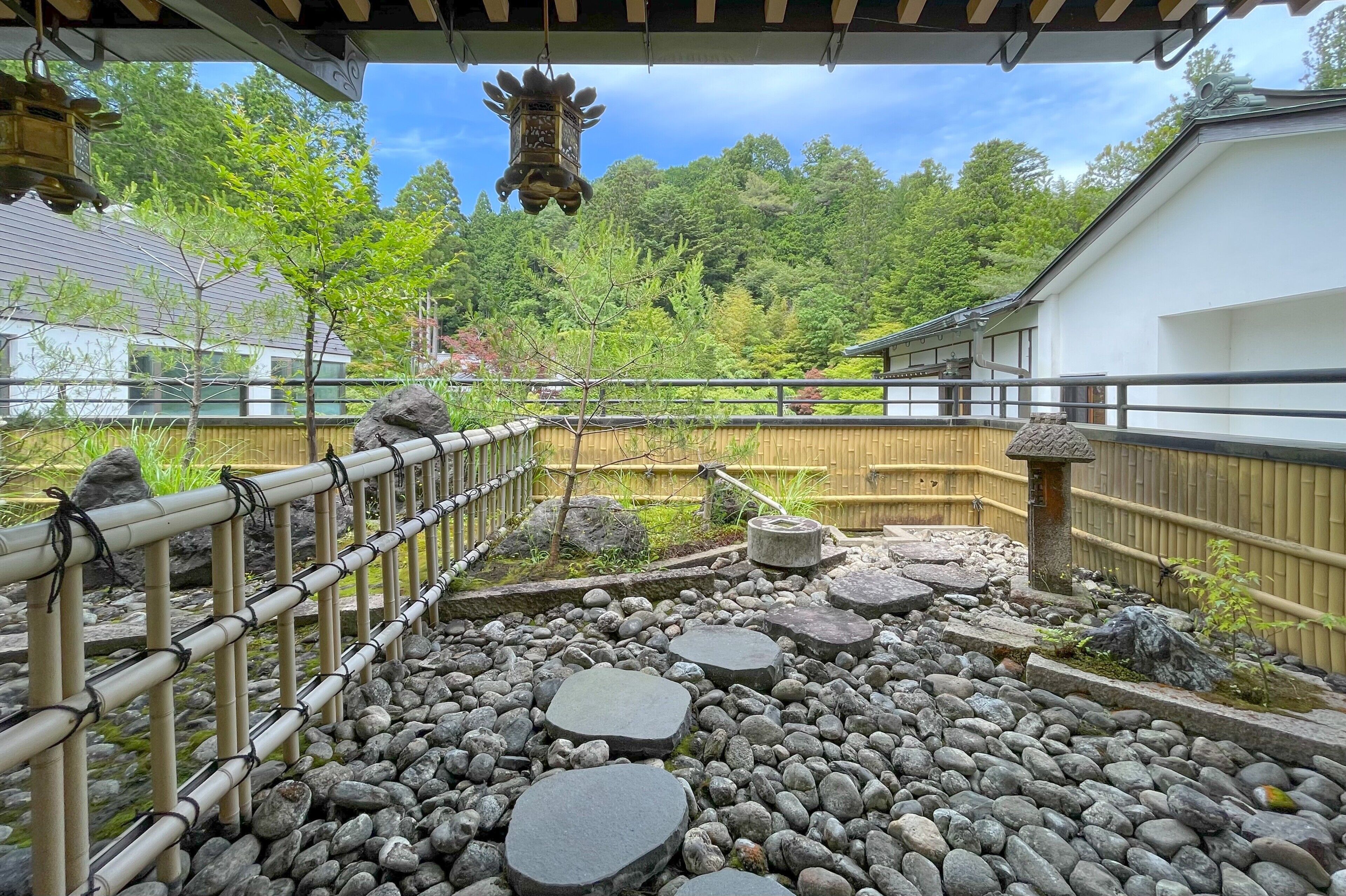 A traditional Japanese garden with a bamboo fence, stepping stones, and a hanging lantern.