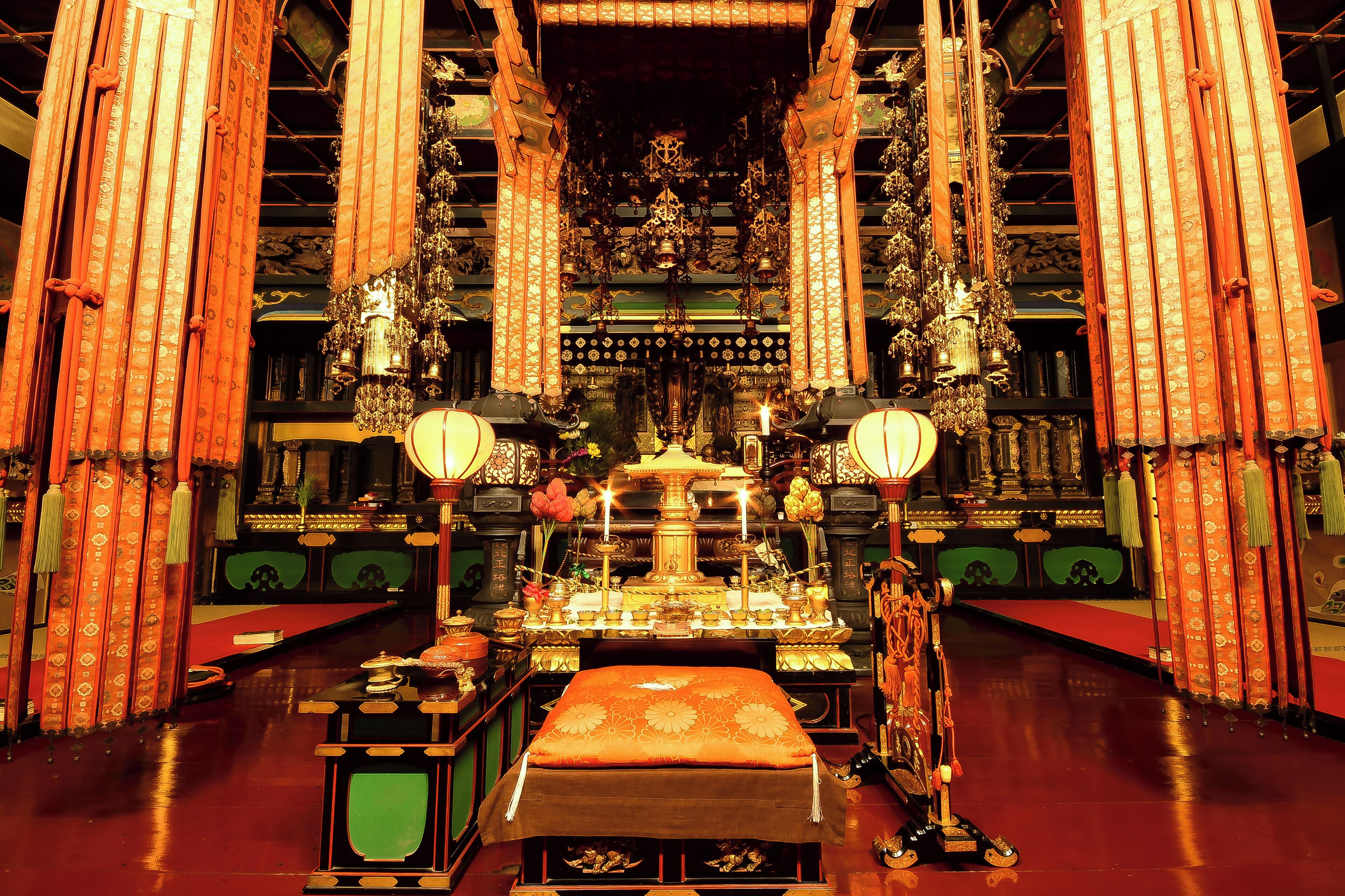 Un interior ornamentado con un altar central, cortinas rojas y candelabros.