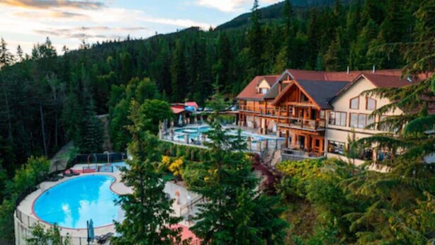 A lodge with a pool, surrounded by forest and mountains. - Halcyon Hot Springs Resort (Nakusp)