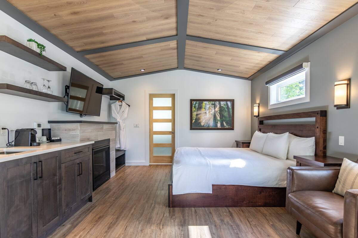A bedroom with a wooden ceiling, a large bed, a nightstand, a dresser, and a window.