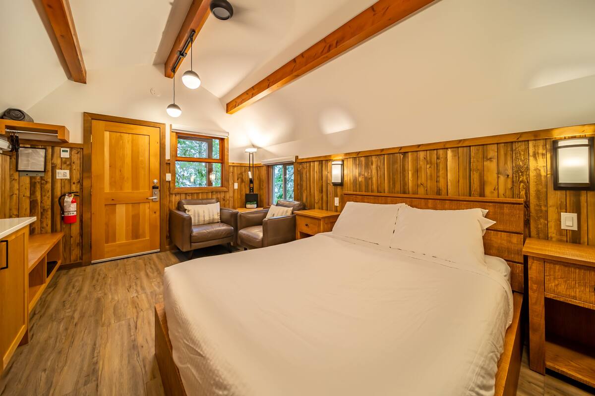 A bedroom with a large bed, wooden walls, a desk, a chair, and a nightstand.