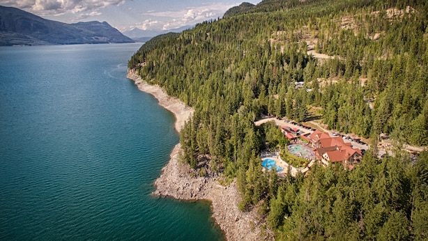 A lakeside resort with a swimming pool, surrounded by dense forest and mountains. - Halcyon Hot Springs Resort (Nakusp)