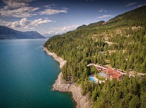A lakeside resort with a swimming pool, surrounded by dense forest and mountains. - Halcyon Hot Springs Resort (Nakusp)