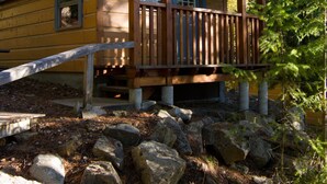 A cabin with a wooden deck, surrounded by rocks and trees. - Halcyon Hot Springs Resort (Nakusp)
