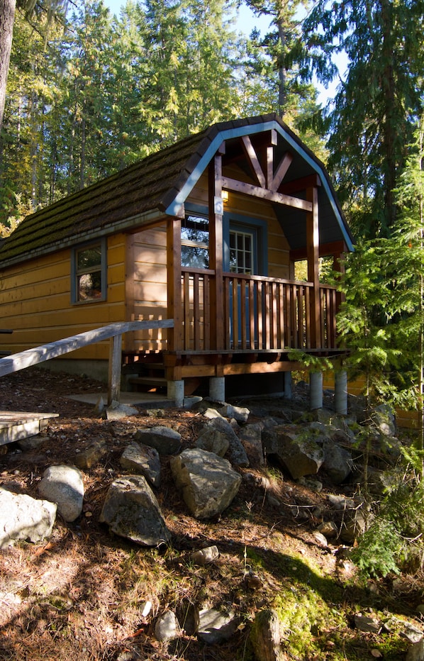 A cabin with a wooden deck, surrounded by rocks and trees.