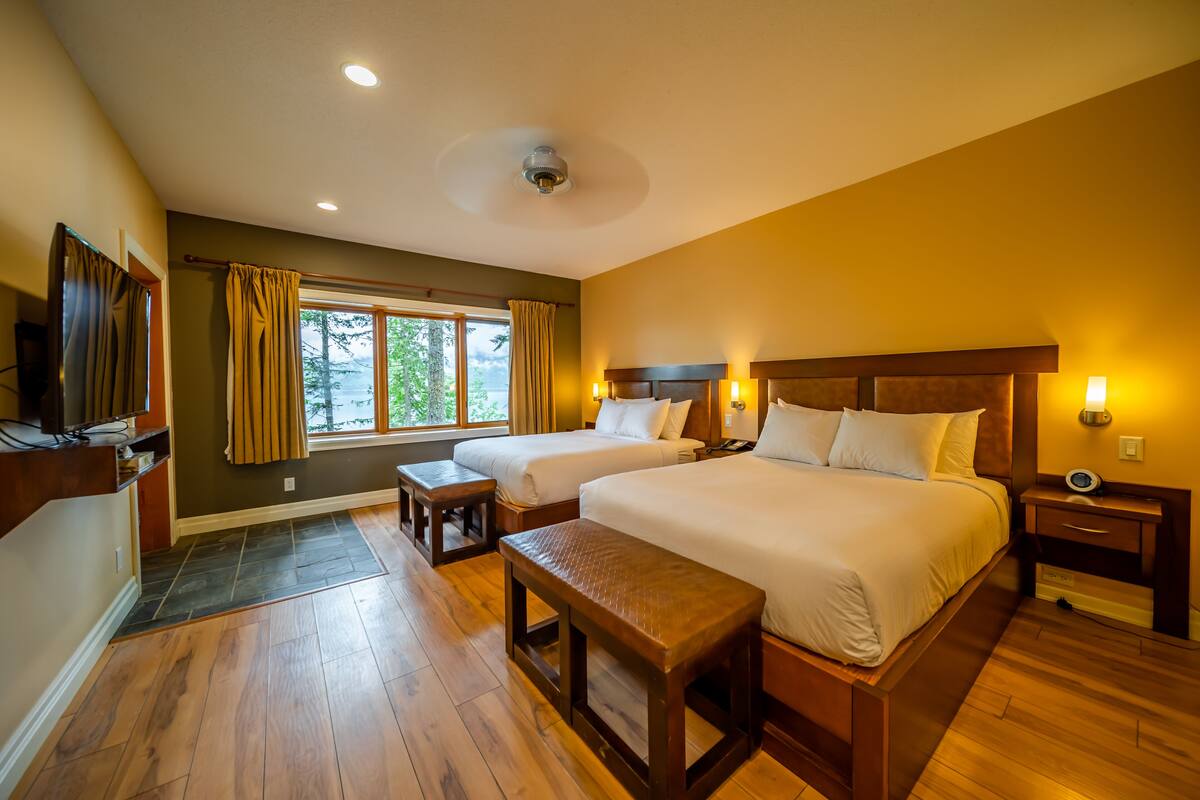 A hotel room with two beds, a wooden bench, a TV, and a window with curtains.