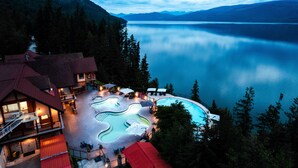 A resort with a swimming pool, outdoor seating, and a view of a lake and mountains. - Halcyon Hot Springs Resort (Nakusp)