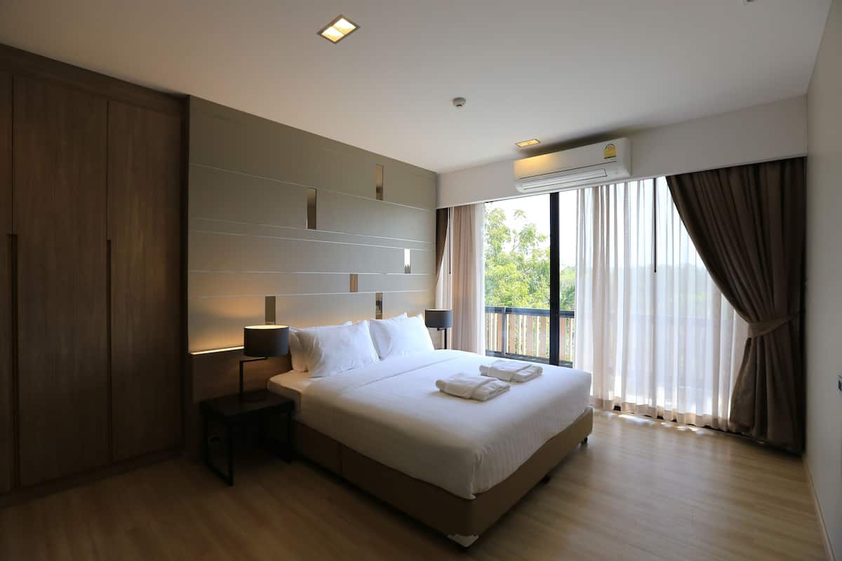 Una habitación de hotel moderna con una cama grande, una mesita de noche, un armario y un balcón con cortinas.
