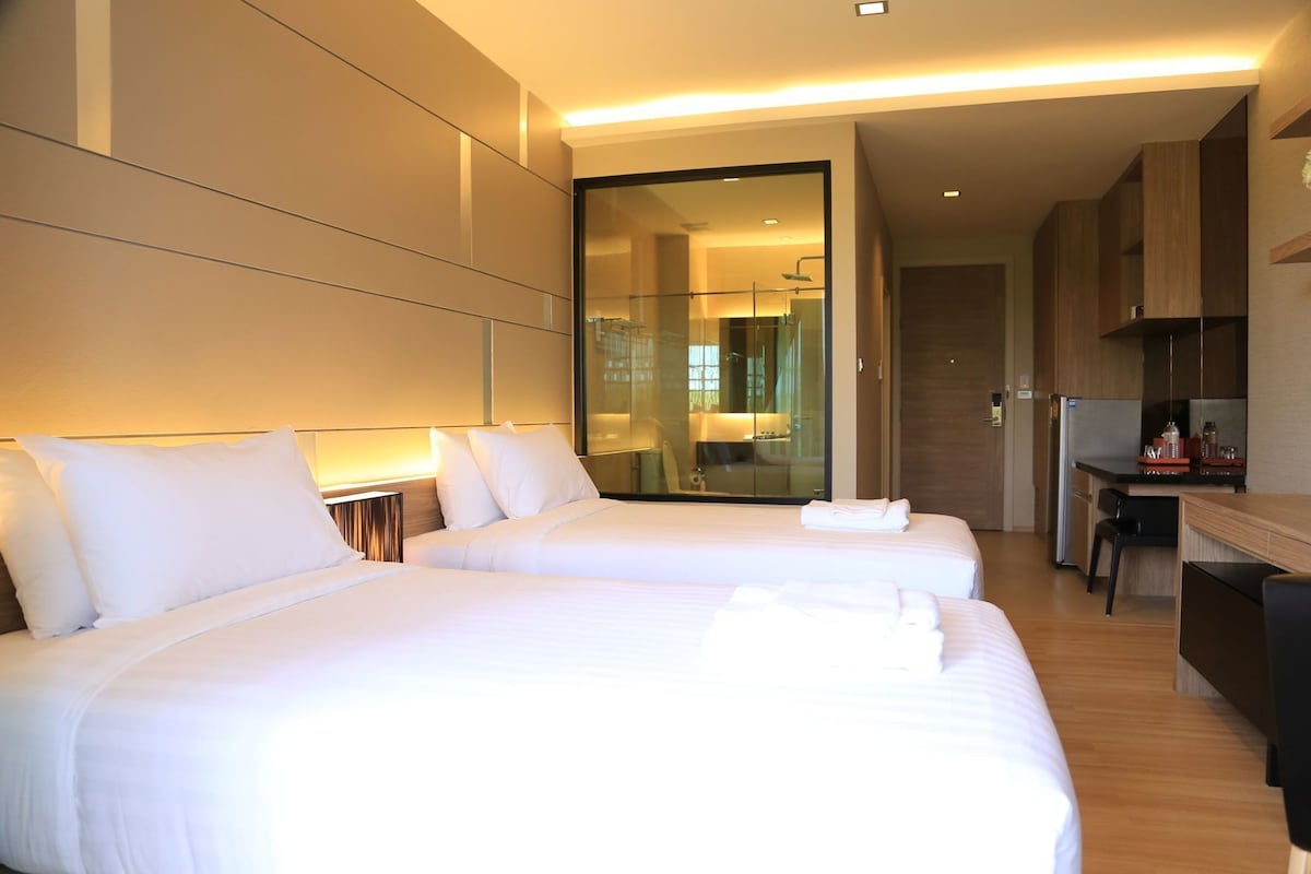 A hotel room with two beds, a desk, a mirror, and a view of the bathroom.