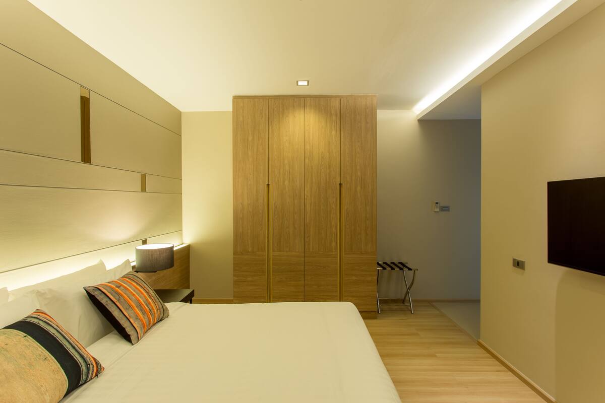 Un dormitorio moderno con una cama grande, un armario, una mesita de noche con lámpara y un televisor montado en la pared.