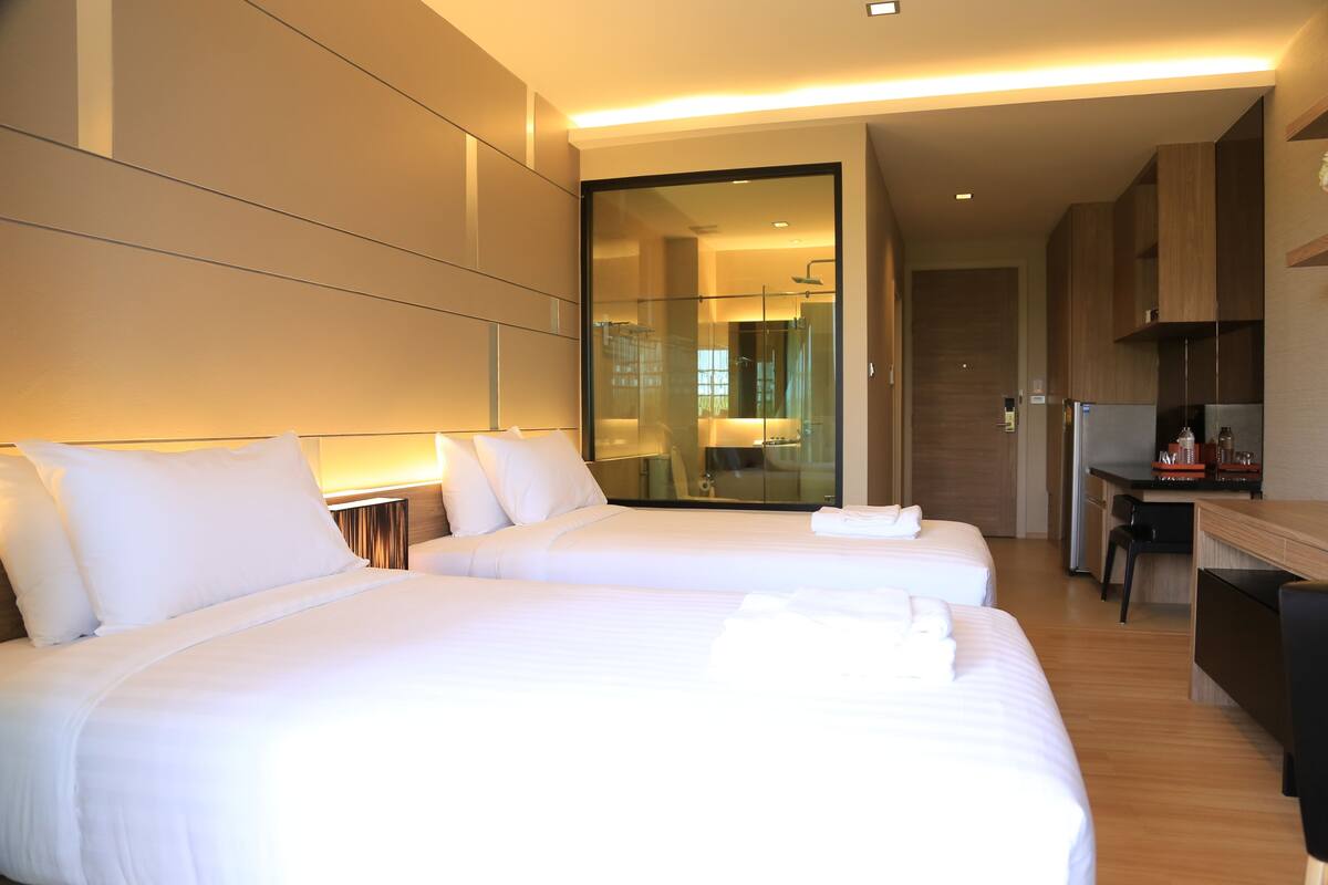 Habitación de hotel moderna con dos camas, un escritorio y cabina de ducha de vidrio.