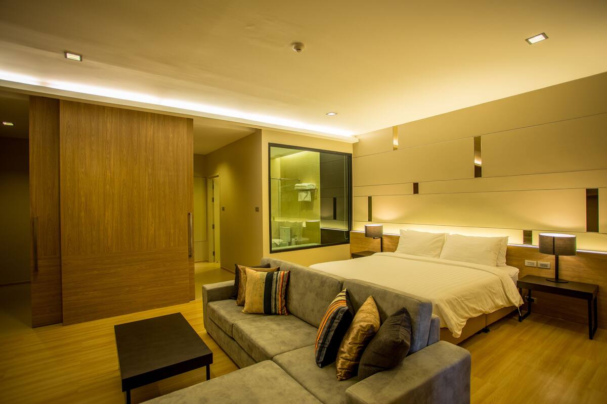Una habitación de hotel moderna con una cama grande, un sofá, una mesita y un espejo.