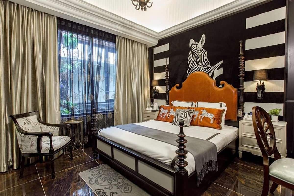 A bedroom with a large bed, a chair, a nightstand, and a wall with a zebra mural.
