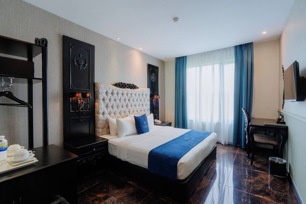 A hotel room with a large bed, a desk, a chair, a TV, and a wardrobe.