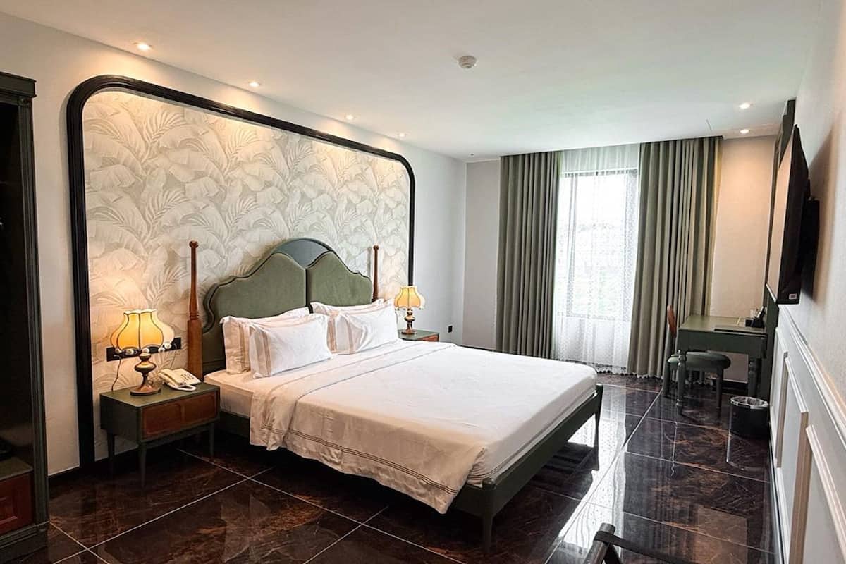 A hotel room with a large bed, two bedside tables with lamps, a desk, and a chair.