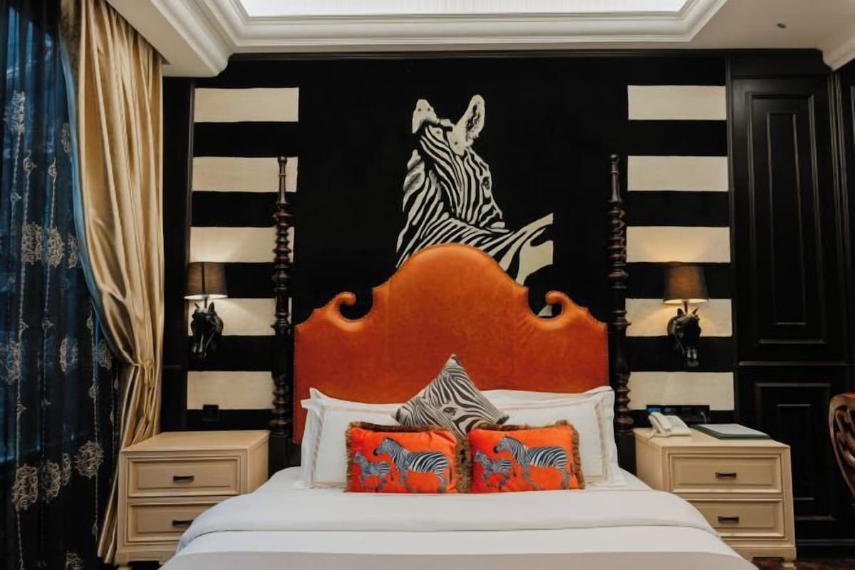 A bedroom with a zebra-themed headboard, a bed with white linens, two nightstands with lamps, and a large zebra mural on the wall.