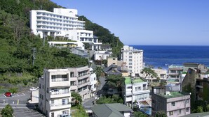A coastal town with a prominent white hotel with multiple floors and balconies, surrounded by smaller buildings and lush greenery. - HOTEL KATARA RESORT&SPA (Higashiizu)