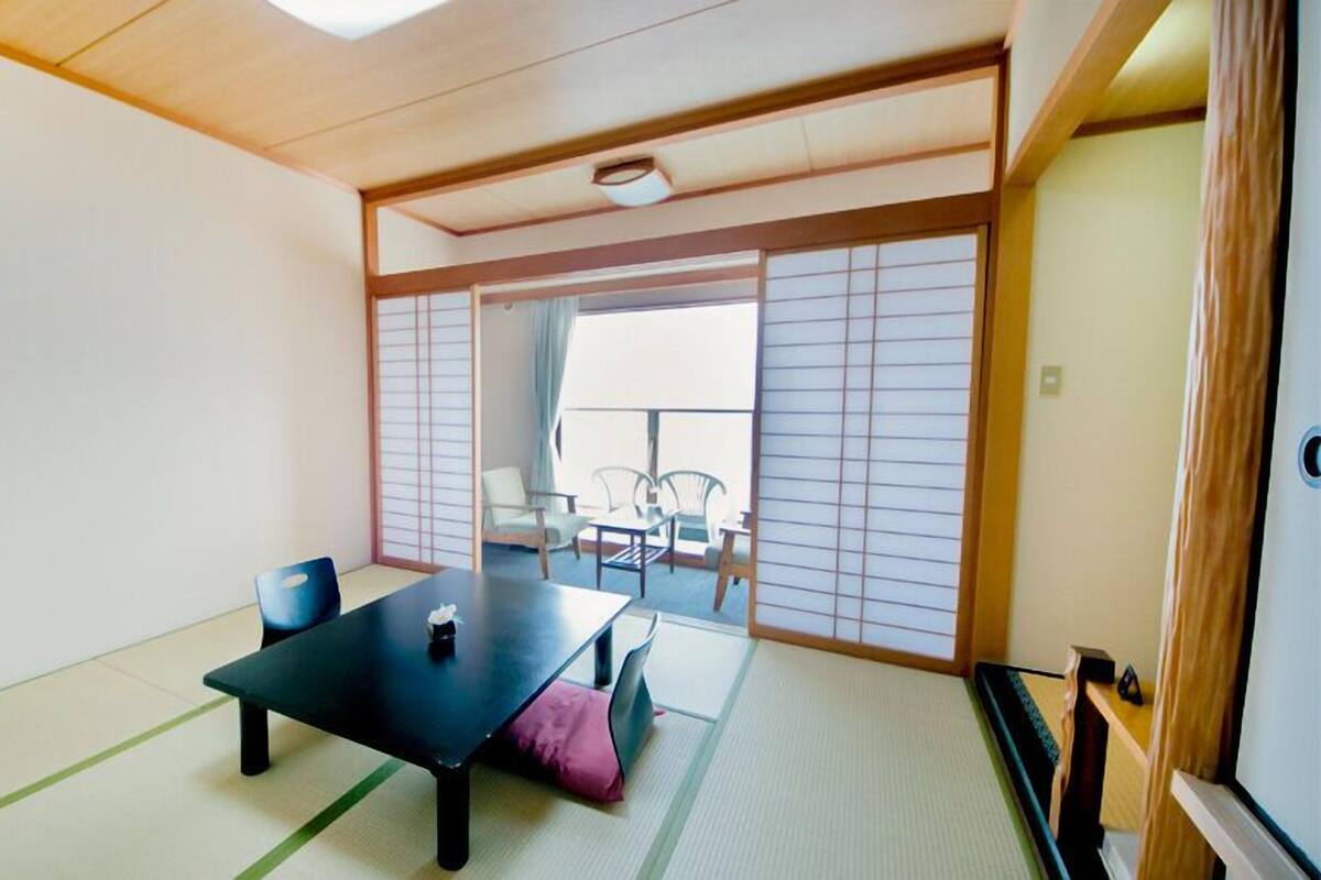 A traditional Japanese room with tatami flooring, a low table, and sliding doors leading to a balcony with outdoor furniture.
