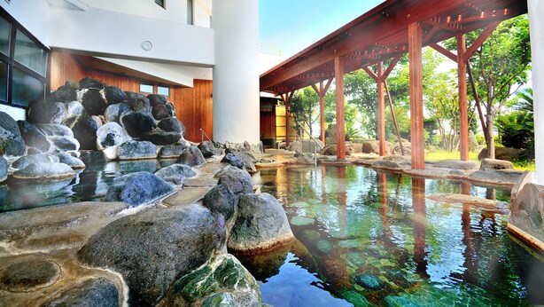 A serene indoor water feature with rocks and a wooden bridge, surrounded by a modern building with large windows and a traditional wooden interior. - HOTEL KATARA RESORT&SPA (Higashiizu)