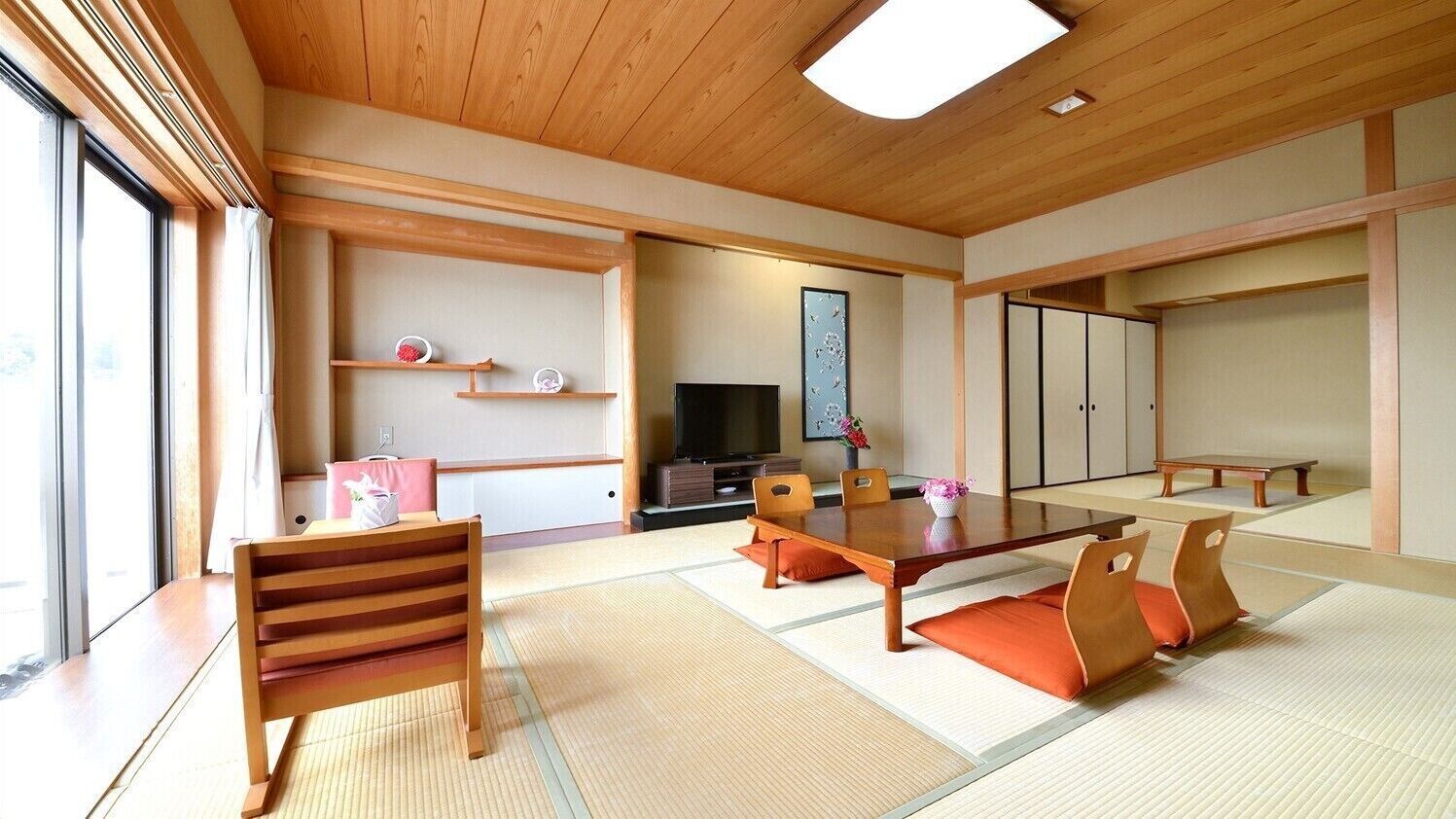 Ein traditioneller japanischer Raum mit Tatami-Boden, einem niedrigen Tisch mit Kissen, einem Fernseher und verschiebbaren Türen.