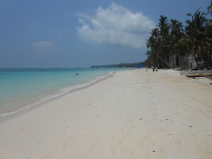 Ein Strand mit weißem Sand, klarem türkisblauem Wasser und Palmen.
